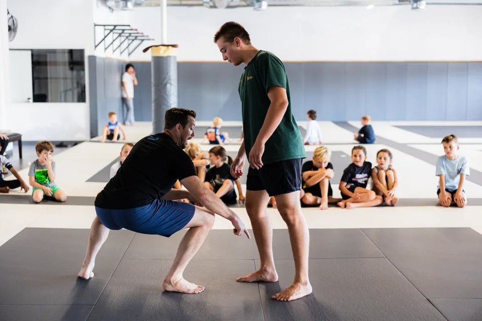 A coach shows a student a stance while children watch