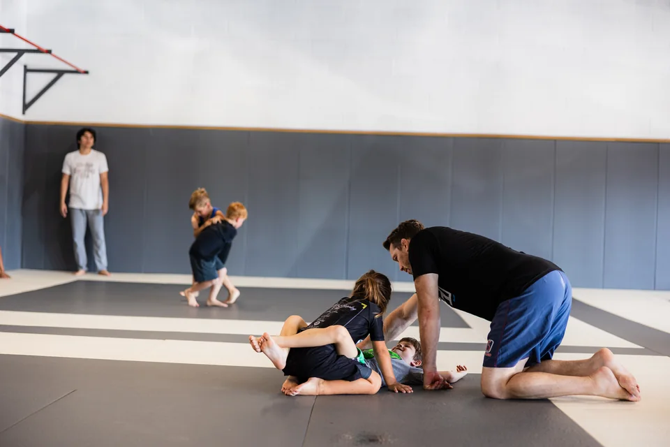 A coach guides two children through a ground position