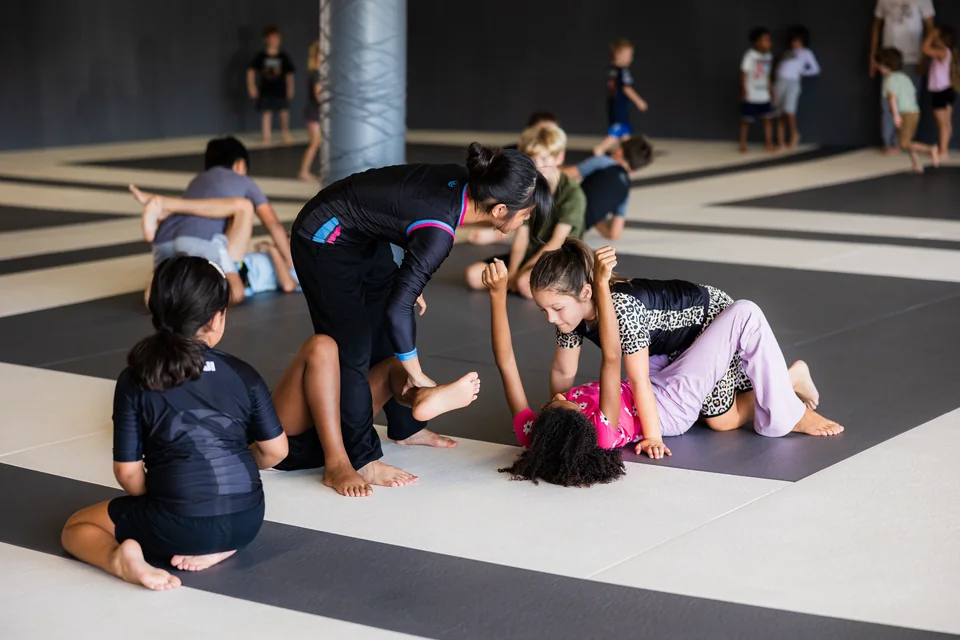 A coach helps children practice a leg position on the mats