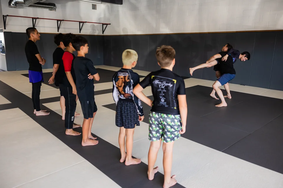 Students watch a no-gi grappling demonstration on the mats