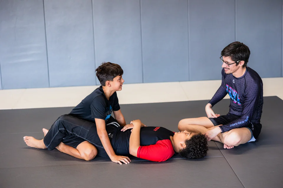 A coach sits with two boys during a grappling drill