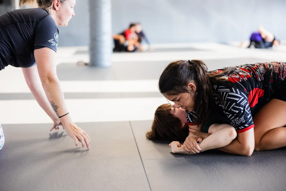 Women practice a grappling position while another woman watches