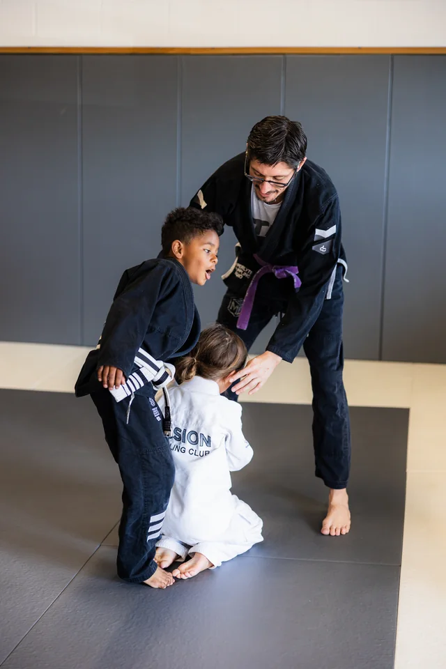 A coach adjusts two students during gi practice