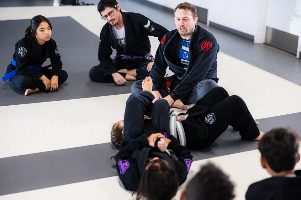 A coach demonstrates a grappling technique while students in gis watch