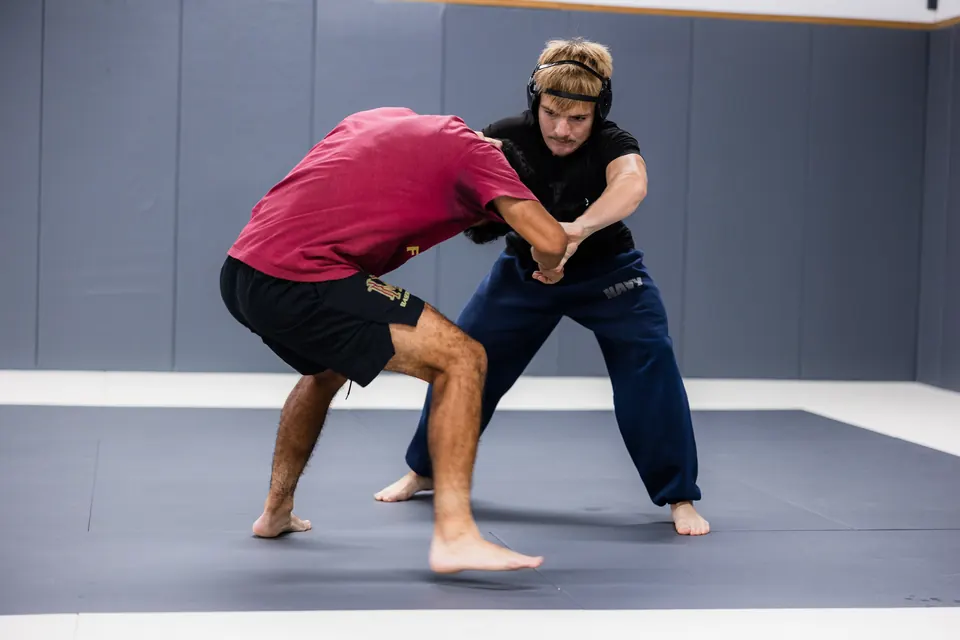 Two students practice a standing wrestling drill on the mats