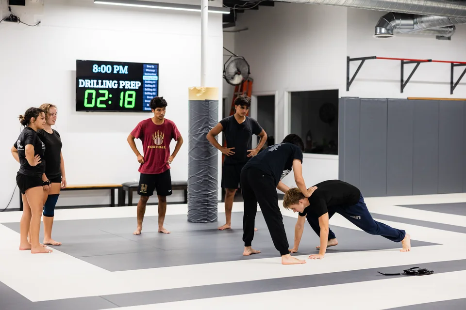 Students drill a grappling position while the class clock shows drilling prep