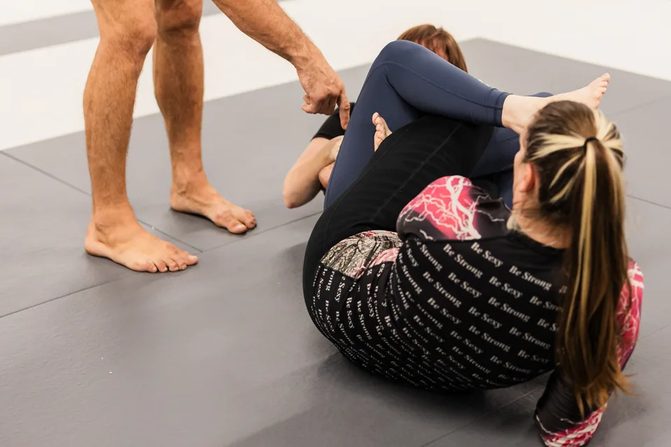 Two women practice a grappling position on the mats