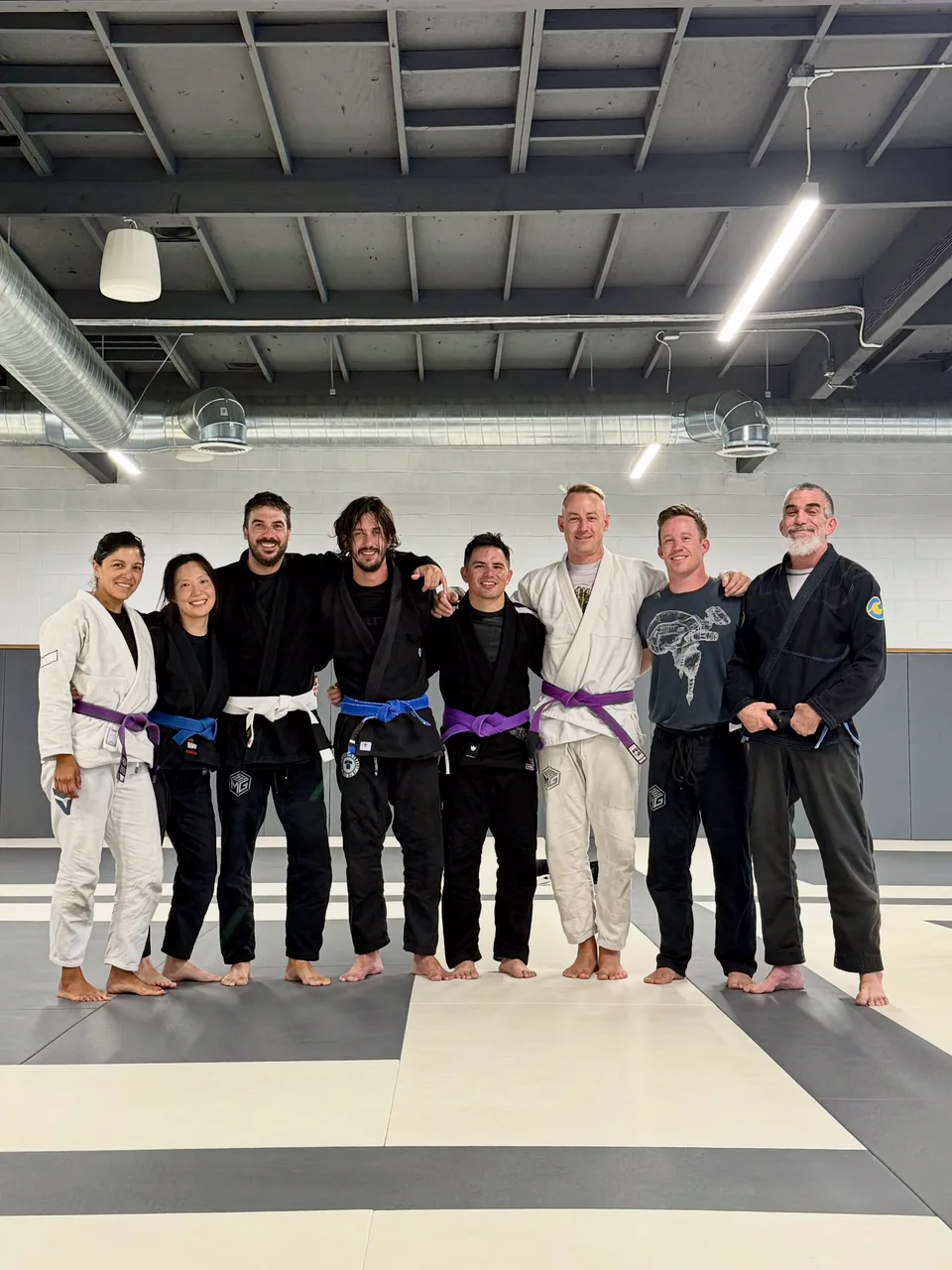 A group of adults in gis stand together on the mats at Mission Grappling Club