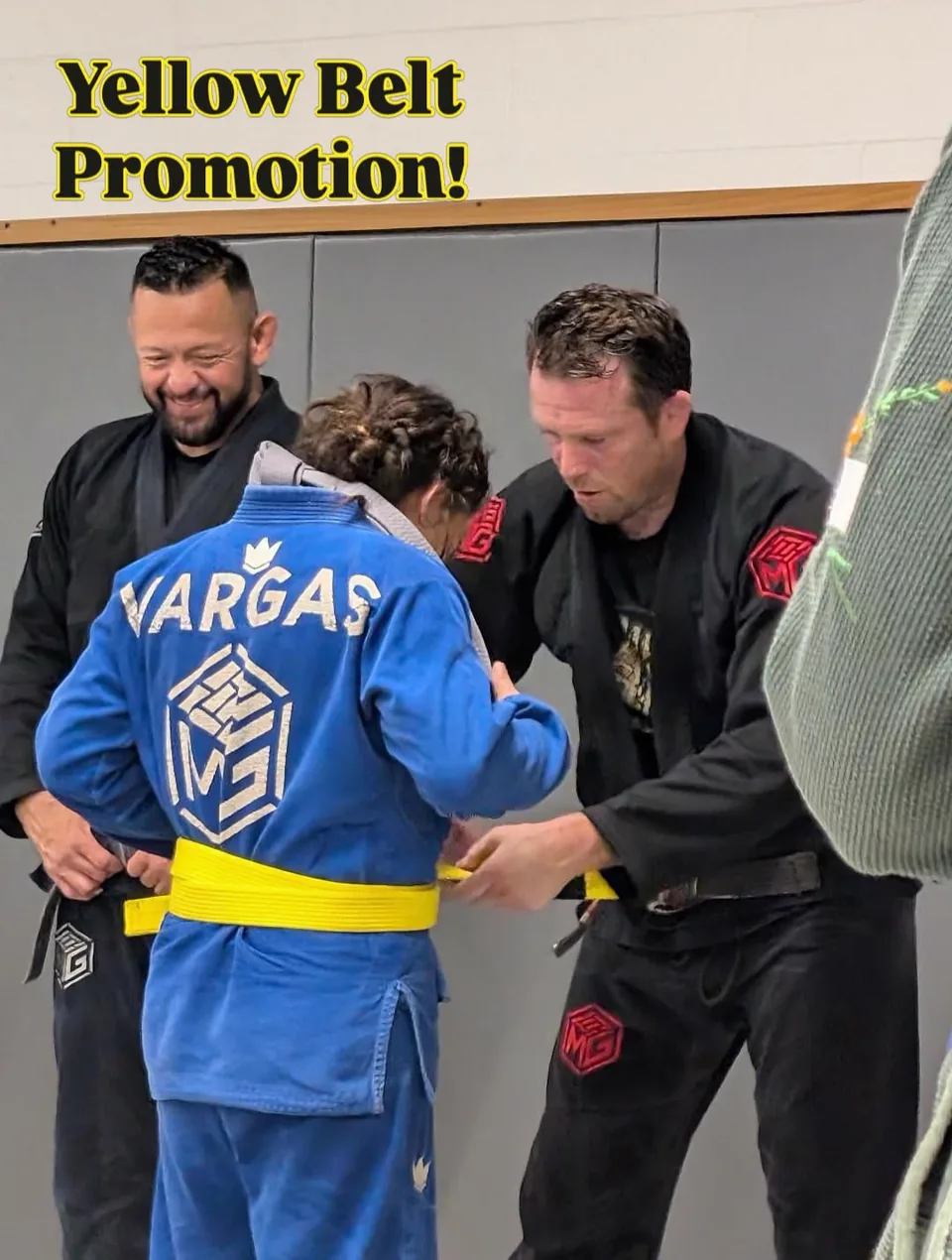 A yellow belt is tied on a student in a blue gi