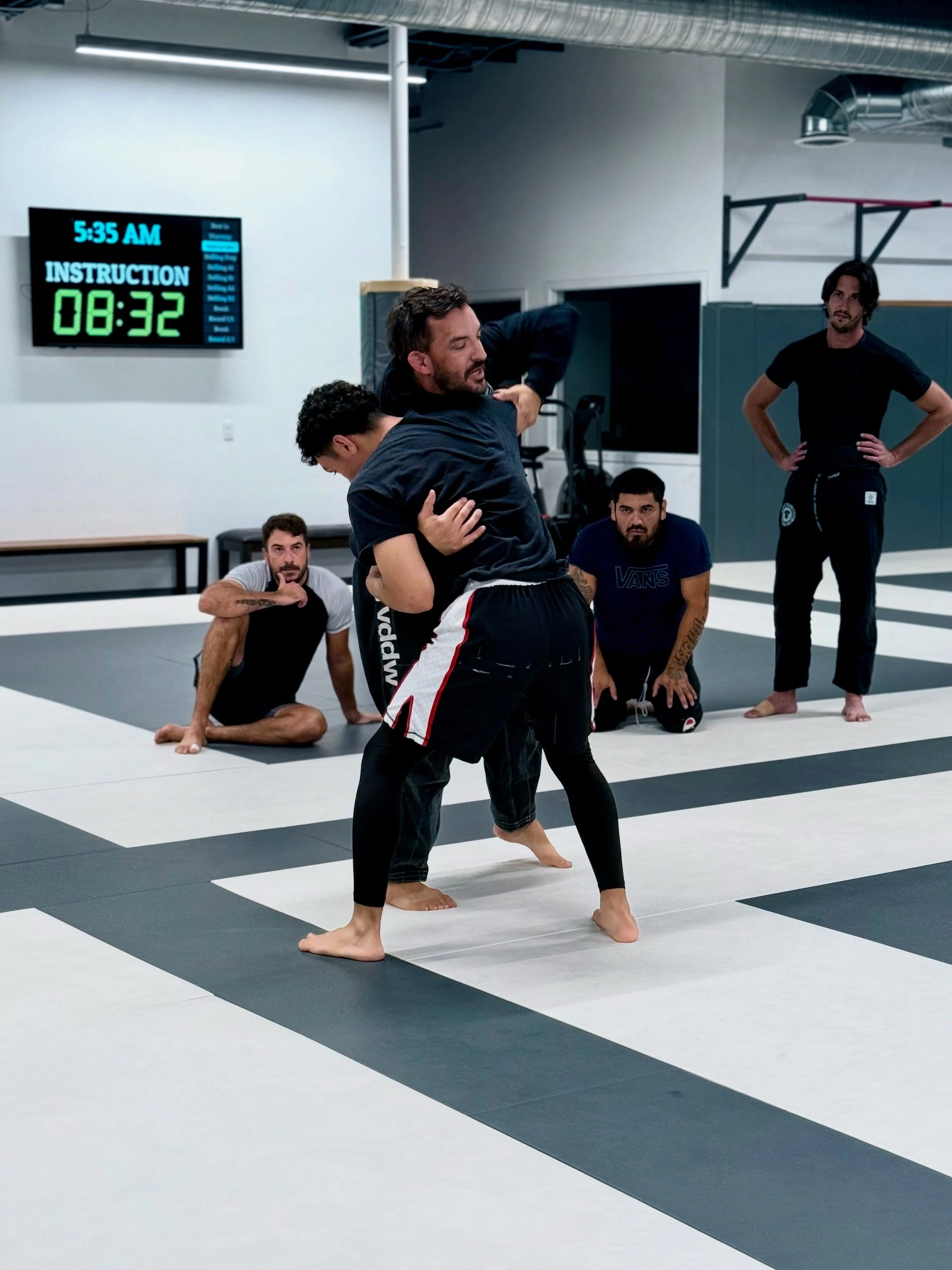 Adult students practicing a takedown during coached grappling instruction